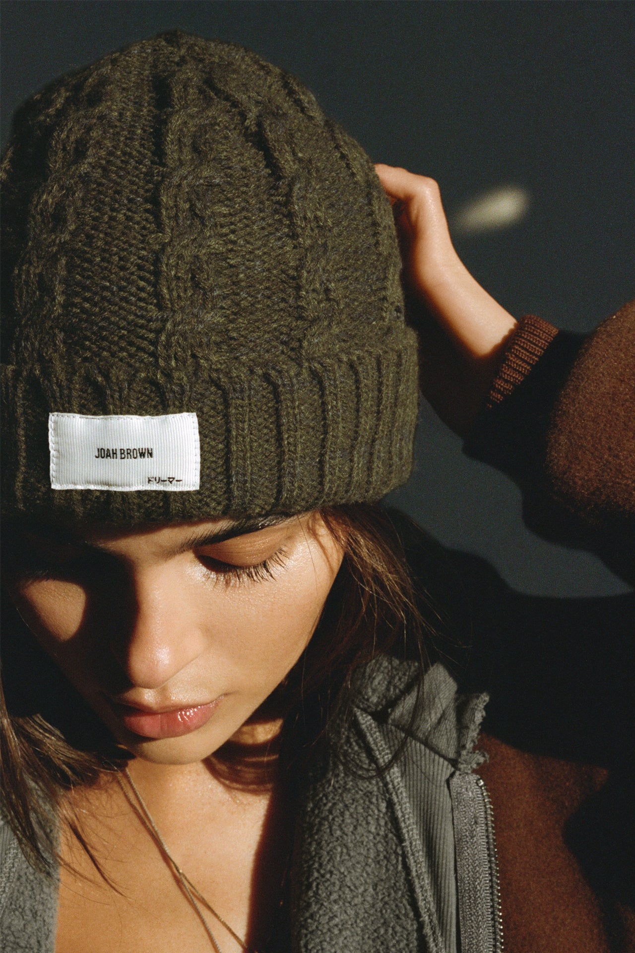 Front view of model posing in the soft and warm moss Cable Knit Beanie that has a custom JOAH BROWN Dreamer logo patch on the front