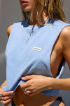 Close up detail side view of model posing in the relaxed fit denim cotton Cut Off Boyfriend Tank with low cut armholes, a crew neckline and a joah brown logo patch at the upper left chest