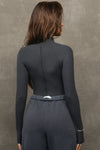 Back view of model posing in the fitted vintage navy flexrib Stitch Mock Neck Long Sleeve top with tonal stitching on the front, a mock neckline and thumbholes in the cuffs