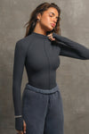 Front view of model posing in the fitted vintage navy flexrib Stitch Mock Neck Long Sleeve top with tonal stitching on the front, a mock neckline and thumbholes in the cuffs