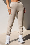 Front view of model from the waist down posing in the tapered sand french terry Empire Jogger with side pockets and an elastic waistband and ankle cuffs