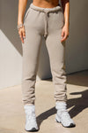 Front view of model from the waist down posing in the tapered sand french terry Empire Jogger with side pockets and an elastic waistband and ankle cuffs