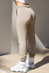 Back view of model from the waist down posing in the tapered sand french terry Empire Jogger with side pockets and an elastic waistband and ankle cuffs