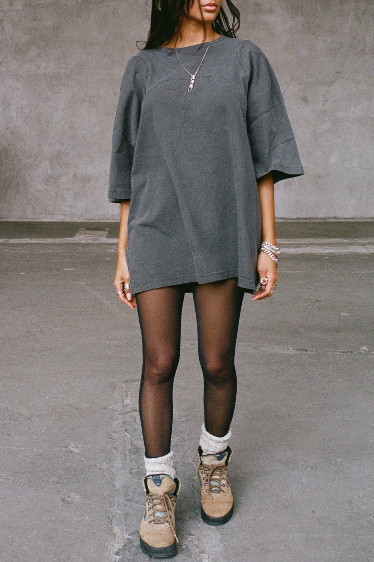 Front view of model posing in the sheer high-waisted black mesh Split Hem Legging with gathered ankles, exposed seams and button closures at the leg opening