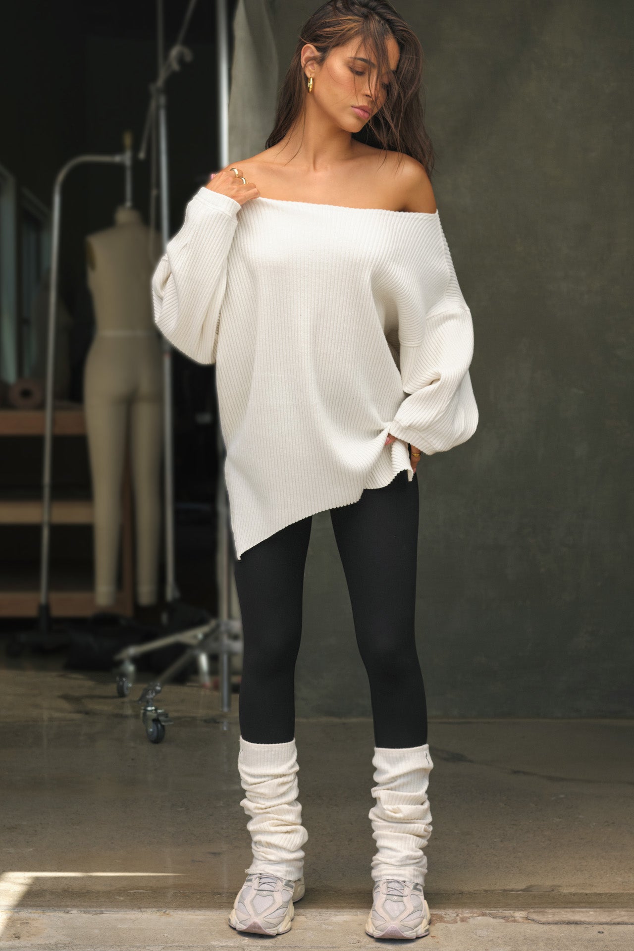 Full body front view of model posing in the relaxed fit natural luxe knit Off Shoulder Tunic with a wide off-the-shoulder neckline and asymmetrical hem