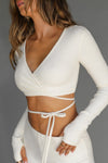 Front view of model posing in the reversible wrap-around ultra cropped natural luxe knit Wrap Cardigan with adjustable ties and fitted sleeves with thumbholes