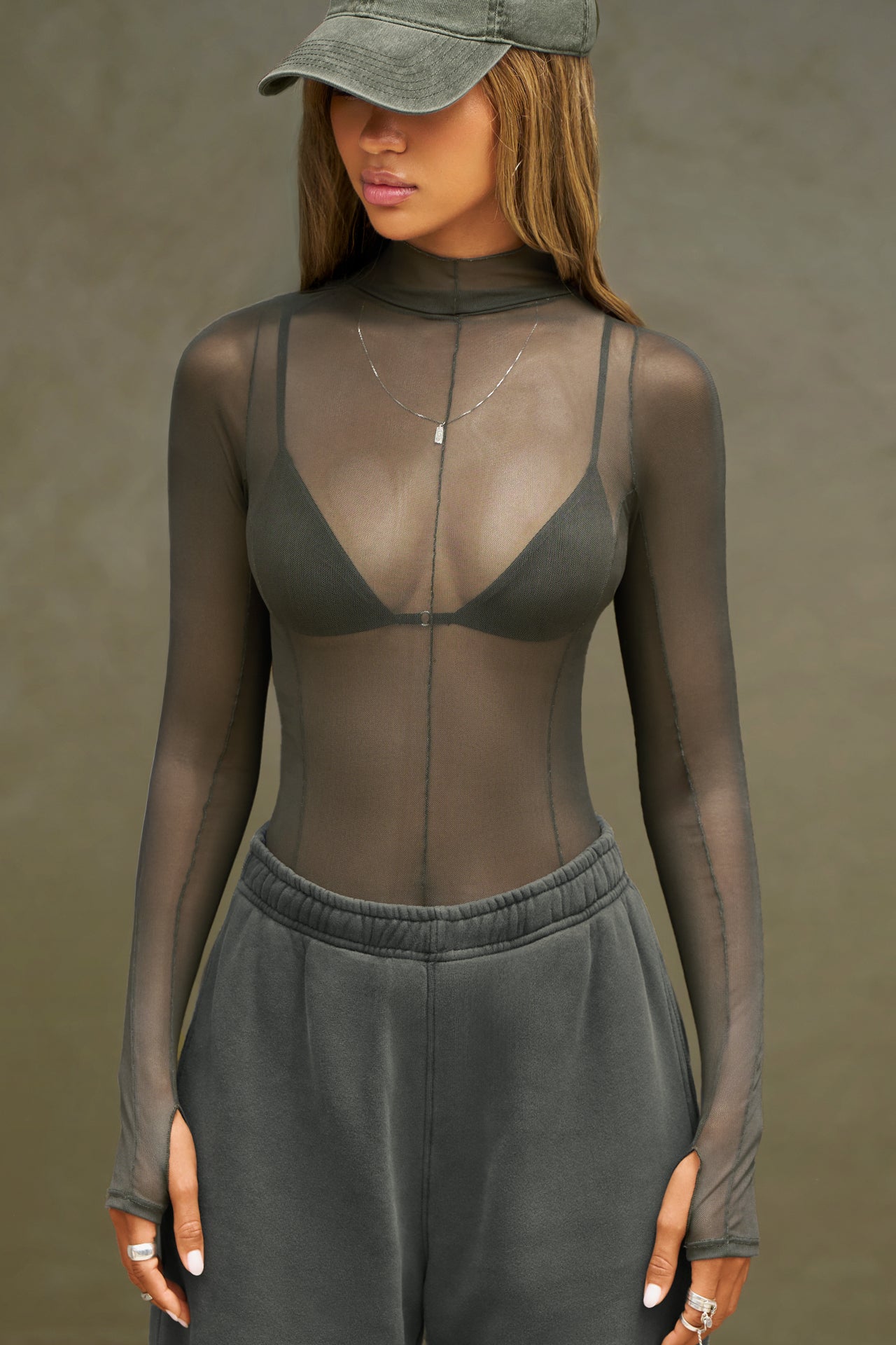 Front view of model posing in the fitted and sheer graphite mesh Exposed Seams Long Sleeve top with a mock neckline and exposed seam details