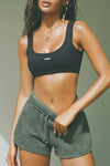 Front view of model posing in the relaxed fit washed sage french terry Sweat Short with side pockets, hidden drawstring, adjustable elastic waistband and a Joah Brown logo patch at the bottom side of the left leg.