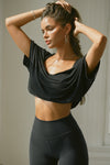 Front view of model posing in the cropped, loose fitting black model Slouchy Crop Tee with a wide scoop neckline