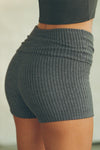 Close up side view of model from the waist down posing in the fitted, soft charcoal luxe knit Foldover Short with a foldover waist band that can be worn high, low or mid-rise
