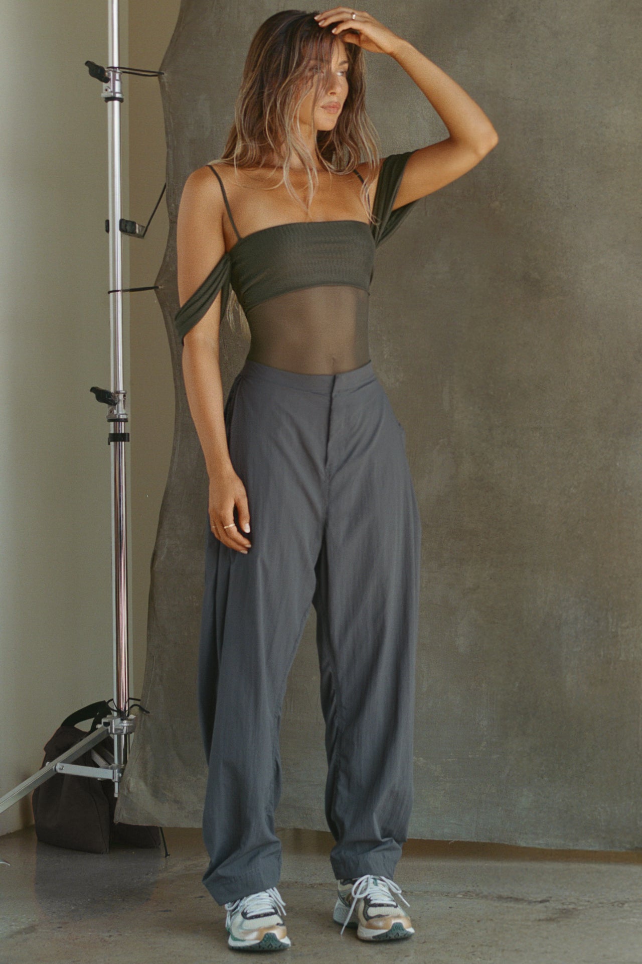 Full body front view of model posing in the sheer and fitted graphite mesh Off The Shoulder Bandeau Tank with thin straps and draped sleeves and can be worn off the shoulder or with the sleeves up