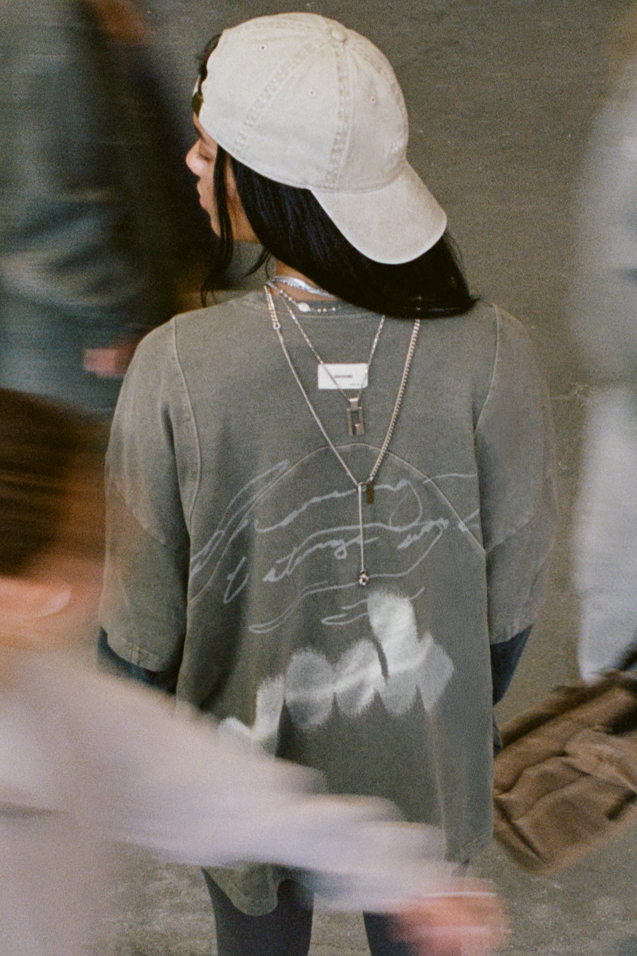 Bird's eye back view of model posing in the oversized haze cotton Original Graphic Tee with panel details and custom screen print graphic dreaming of a strange world on the back