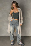 Full body front view of model posing in the knee-length loose fitting sand sherpa Oversized Cardigan with a rolled neckline and extra long sleeves
