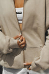 Close up detail front view of model posing in the oversized comfortable sand french terry Oversized Zip Hoodie with a full length front zip closure, side pockets and thumbholes in the fitted cuffs