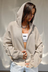 Front view of model posing in the oversized comfortable sand french terry Oversized Zip Hoodie with a full length front zip closure, side pockets and thumbholes in the fitted cuffs