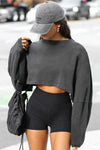 Front view of model posing in the cropped relaxed fit washed black cotton slouchy crop long sleeve top with a crew neckline, dropped shoulders and oversized sleeves