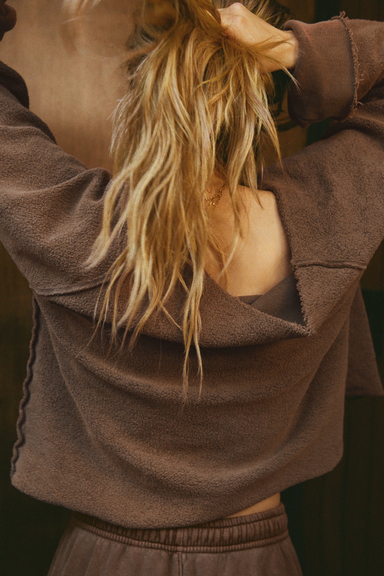 Back view of model posing in the oversized cedar french terry Slouchy Pullover Sweatshirt with a wide, off-the-shoulder neckline and a JOAH BROWN logo patch on the right sleeve, which she is wearing inside out
