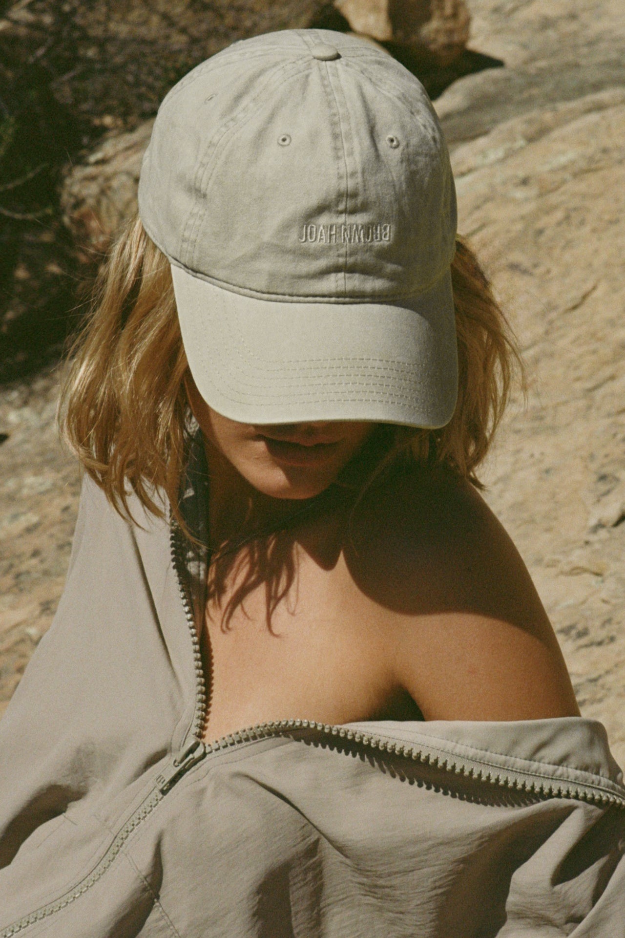 Front view of model posing outside wearing the six-panel sahara Official Cap with a curved brim and an embroidered upside down Joah Brown logo on the front