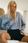 Front view of model posing in the cropped, loose-fitting denim cotton Vintage Henley Long Sleeve top with dropped shoulders and custom JOAH BROWN buttons