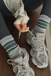 Close up front view of model adjusting the crew-style ribbed and soft heathered charcoal Merino Stripe Sock