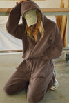 Front view of model in a kneeling position posing in the oversized comfortable cedar french terry Oversized Zip Hoodie with a full length front zip closure, side pockets and thumbholes in the fitted cuffs