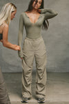 Full body front view of model posing in the relaxed fit, desert sage nylon Ruched Track Pant with a wide leg, side ruched panels and finished with a drawcord waist, side pockets and adjustable button closures at the ankle.