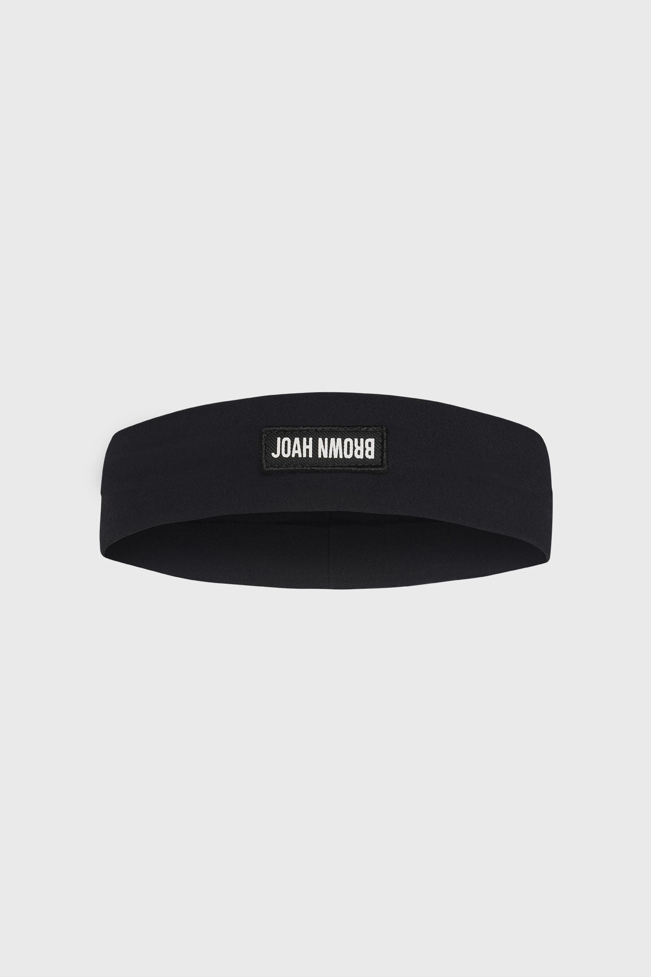 Flat lay front view of the stretchy wide sueded onyx Classic Headband with a Joah Brown logo patch on the front