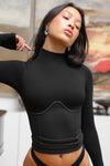 Front view of model posing in the fitted stretchy vintage black flexrib Corset Long Sleeve top with a mock neckline, modal top half and ribbed bottom half with corset-style seaming at the bodice