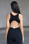 Back view of model posing in the fitted cropped black flexrib Curve Crop Tank wih a vertical stitch detail down the front, a curved hemline in an inverted u-shape and a high v-neckline