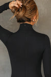 Close up back view of model posing in the fitted black rib Mock Neck Midi Dress with a mock turtleneck neckline, long sleeves, quarter zip back and a mid-calf length
