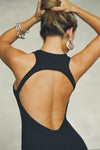Close up back view of model posing in the mini, fitted black rib Open Back Dress with a low scoop neckline and open back