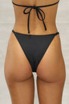Close up back view of model from the waist down posing in the low-rise ink Triangle Bikini Bottom with adjustable side straps, cheeky back and high-cut leg opening.