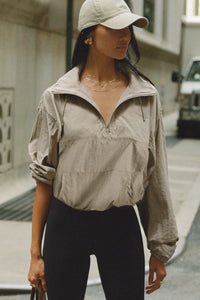 Front view of model posing in a city street in the relaxed fit desert sage nylon 3/4 Zip Windbreaker jacket with a structured collar and 3/4 zip neckline