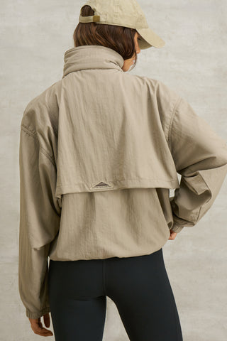 Back view of model posing in the relaxed fit desert sage nylon 3/4 Zip Windbreaker jacket with a structured collar and 3/4 zip neckline