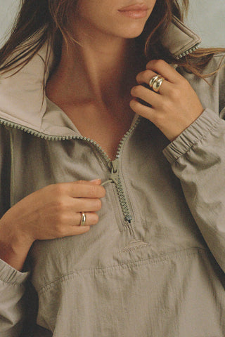 Close up detail front view of model posing in the relaxed fit desert sage nylon 3/4 Zip Windbreaker jacket with a structured collar and 3/4 zip neckline