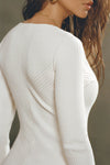 Close up detail back view of model posing in the soft and fitted natural luxe knit Asymmetrical Button Mini Dress with long sleeves,  a v-neckline and asymmetrical button-front details. 