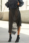 Front view of model from the waist down posing in the lightweight black mesh Asymmetrical Button Skirt with a draped silhouette, asymmetrical hemline and functional side button details for an adjustable fit