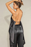 Back view of model posing the flowy iron Asymmetrical Silk Tank with a V-neckline, asymmetrical hem and an open back with thin, versatile straps that can tie straight or crisscross at the back