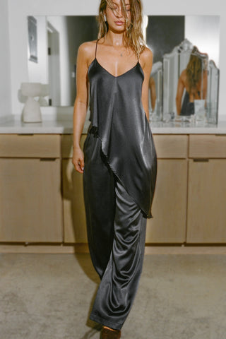 Full body front view of model posing the flowy iron Asymmetrical Silk Tank with a V-neckline, asymmetrical hem and an open back with thin, versatile straps that can tie straight or crisscross at the back