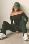 Front view of model posing in the fitted, slightly cropped black modal Bare Shoulder Long Sleeve top with a straight, off-the-shoulder neckline