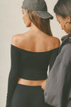 Back view of model posing in the fitted, slightly cropped black modal Bare Shoulder Long Sleeve top with a straight, off-the-shoulder neckline