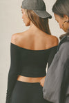 Back view of model posing in the fitted, slightly cropped black modal Bare Shoulder Long Sleeve top with a straight, off-the-shoulder neckline