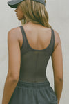 Back view of model posing in the reversible full-length sheer graphite mesh Bare Tank wearing it reversed so the back features a scoop back, with a vertical seam detail down the middle