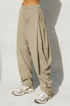 Side view of model from the waist down posing in the oversized, horseshoe-style desert sage nylon Barrel Pant with side pockets, zip fly, pleated sides and adjustable snap closures at the ankle.