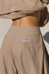 Close up detail back view of model from the waist down posing in the oversized, horseshoe-style fawn nylon Barrel Pant with side pockets, zip fly, pleated sides, adjustable snap closures at the ankle and a JOAH BROWN logo on the back below the waistline.
