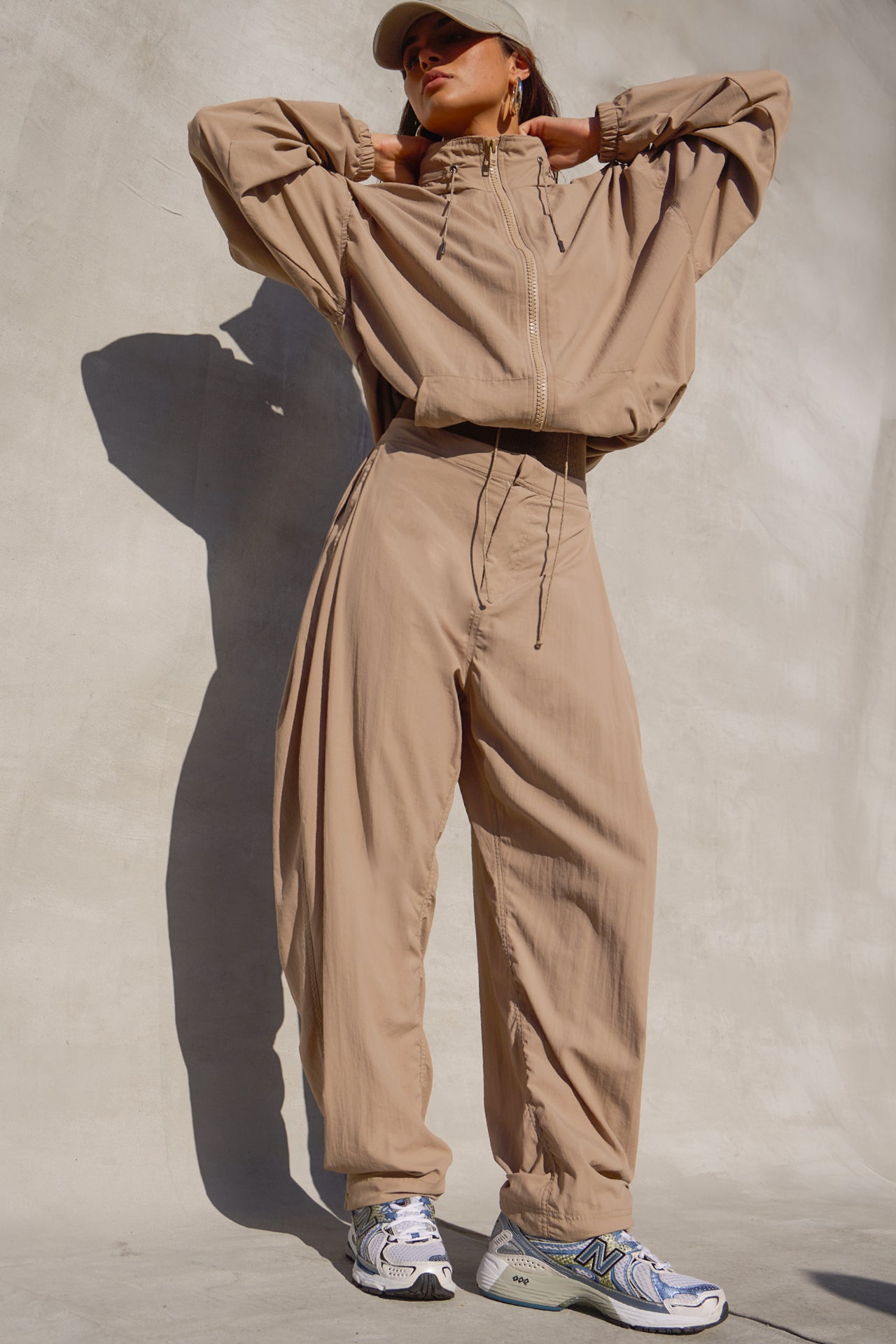 Full body front view of model posing in the oversized, horseshoe-style fawn nylon Barrel Pant with side pockets, zip fly, pleated sides and adjustable snap closures at the ankle.