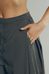 Close up detail front view of model from the waist down posing with her hands in the pocket of the oversized, horseshoe-style jet nylon Barrel Pant with side pockets, zip fly, pleated sides and adjustable snap closures at the ankle.