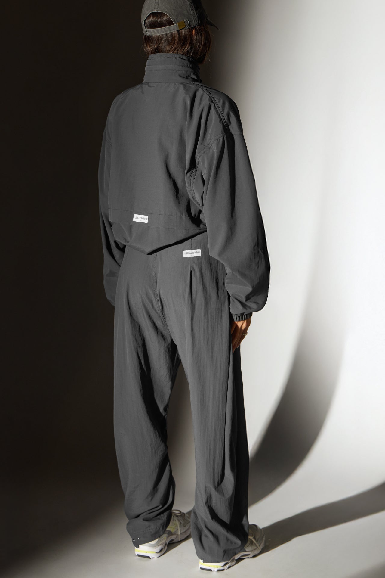 Full body back view of model posing in the oversized, horseshoe-style jet nylon Barrel Pant with side pockets, zip fly, pleated sides, adjustable snap closures at the ankle and a JOAH BROWN logo on the back below the waistline.