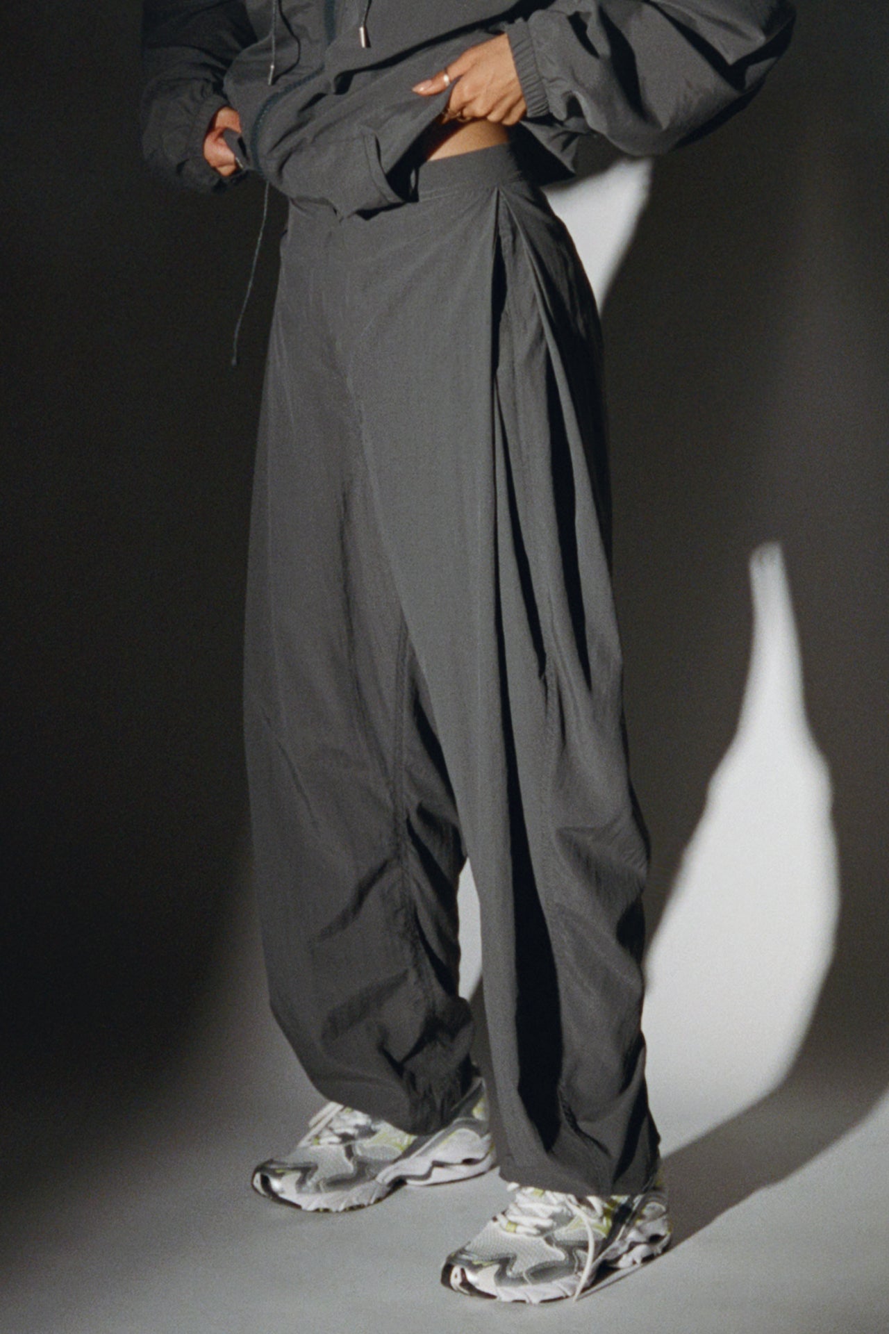 Side view of model from the waist down posing in the oversized, horseshoe-style jet nylon Barrel Pant with side pockets, zip fly, pleated sides and adjustable snap closures at the ankle.