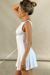 Side view of model posing in the sleeveless white modal Boatneck Mini Dress with a boat neckline, scoop back and fitted A-line silhouette.